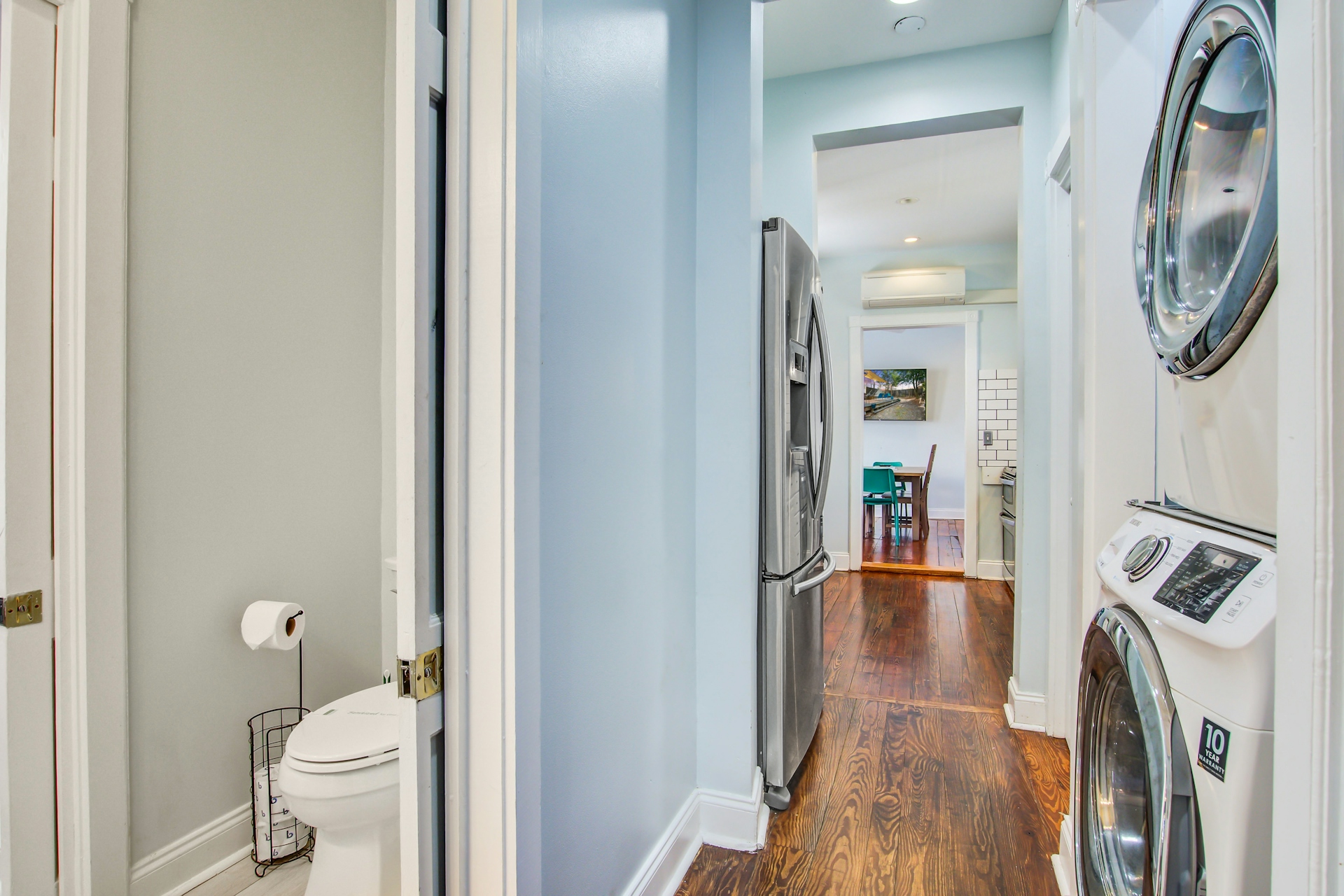 Hallway with stacked white front-load washer and dryer, half bathroom on one side, and views toward kitchen and dining room.