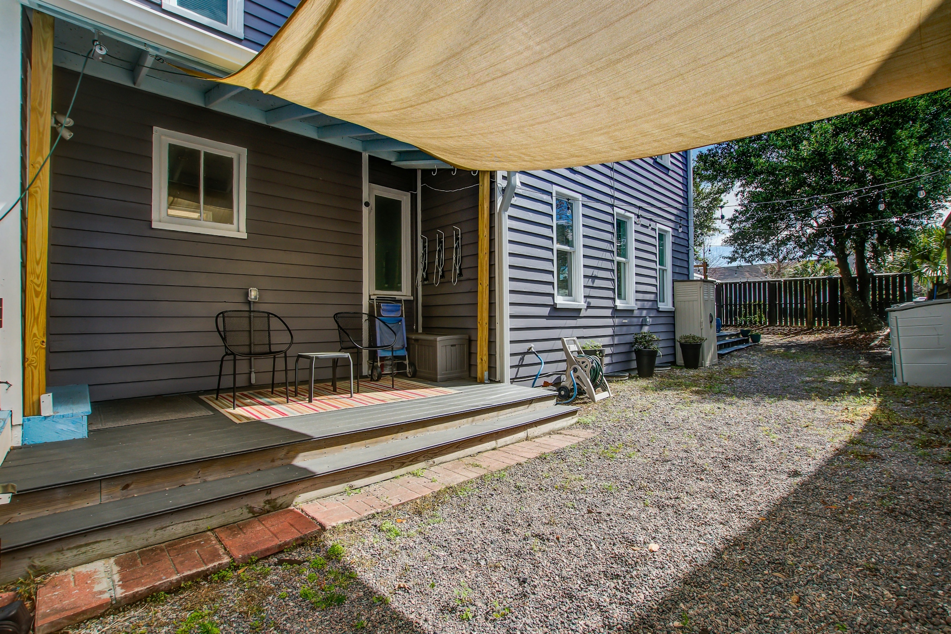 Wider view of side porch and gravel yard: deck, chairs, side entry door, and neighboring houses.
