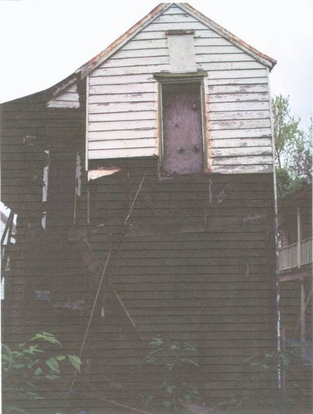Rear gable elevation, showing failed siding and a boarded second-story door.