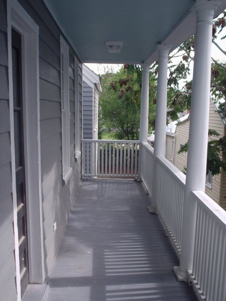 Looking down the restored upper side porch: tongue-and-groove ceiling, square columns, painted floor.