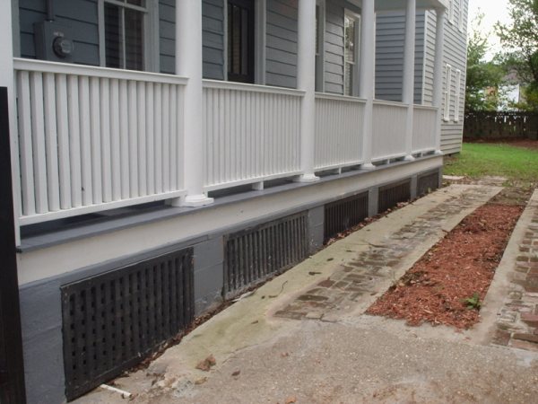 Finished porch skirt with restored cast-iron foundation vents and brick walkway.
