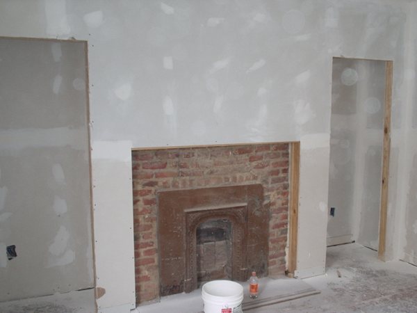Parlor fireplace mid-construction: new drywall around the original brick firebox and cast-iron insert.