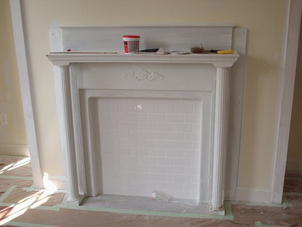 Second fireplace finished with fluted column mantel and white subway-tile surround.