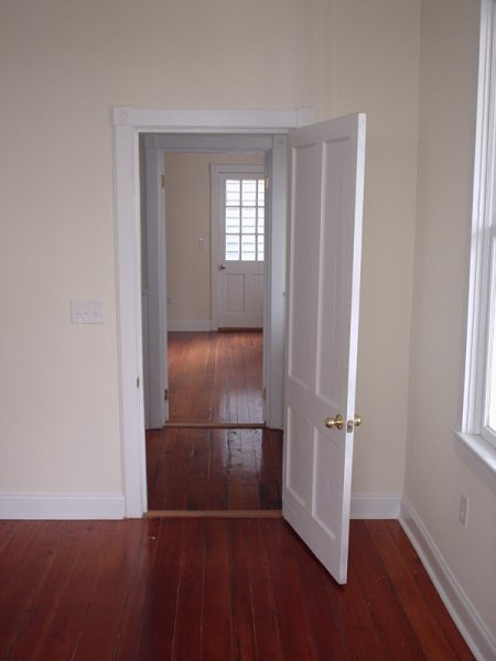 Same arched doorway restored, looking through a six-panel door to a finished bedroom.